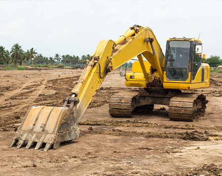 A yellow excavator with a large bucket arm parked on a muddy construction site.