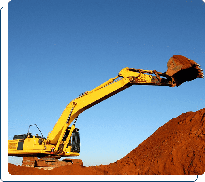 A yellow excavator operating on a mound of red soil against a clear blue sky.