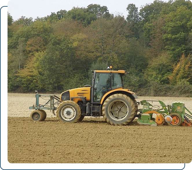 Yellow tractor plowing a field with attached green machinery.