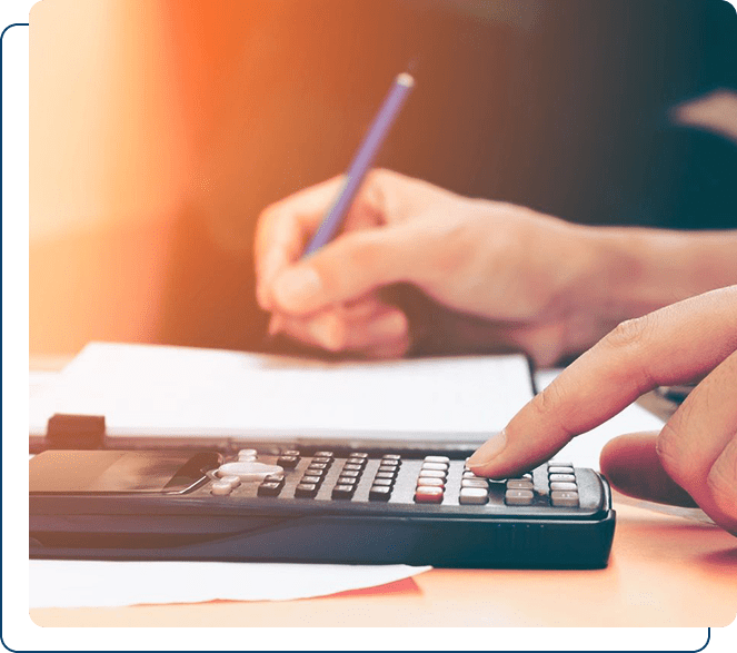 Person using a calculator and writing notes with a pen, sitting at a desk.