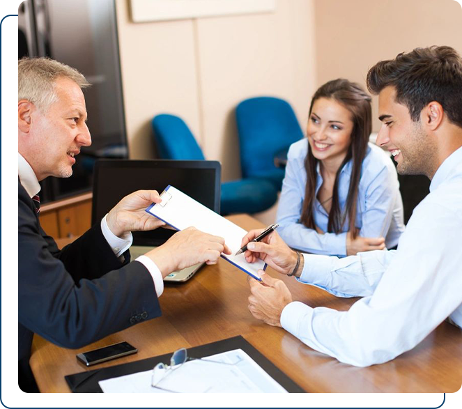 Three professionals sitting at a table, with the older man handing a document to the younger man.