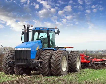 Blue tractor with large tires plowing a field under a clear sky.