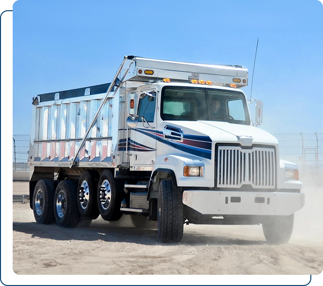 A white and blue dump truck with a loaded bed, parked on a dusty road.